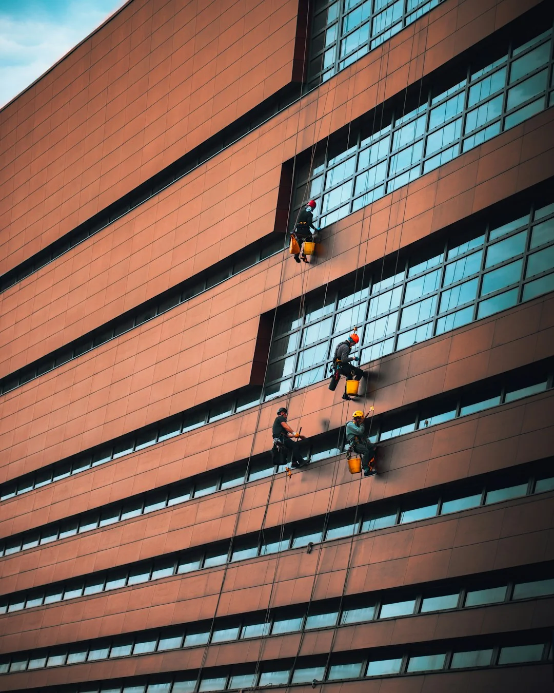 A man wearing a blue t-shirt is cleaning a large glass pane indoors with a squeegee.